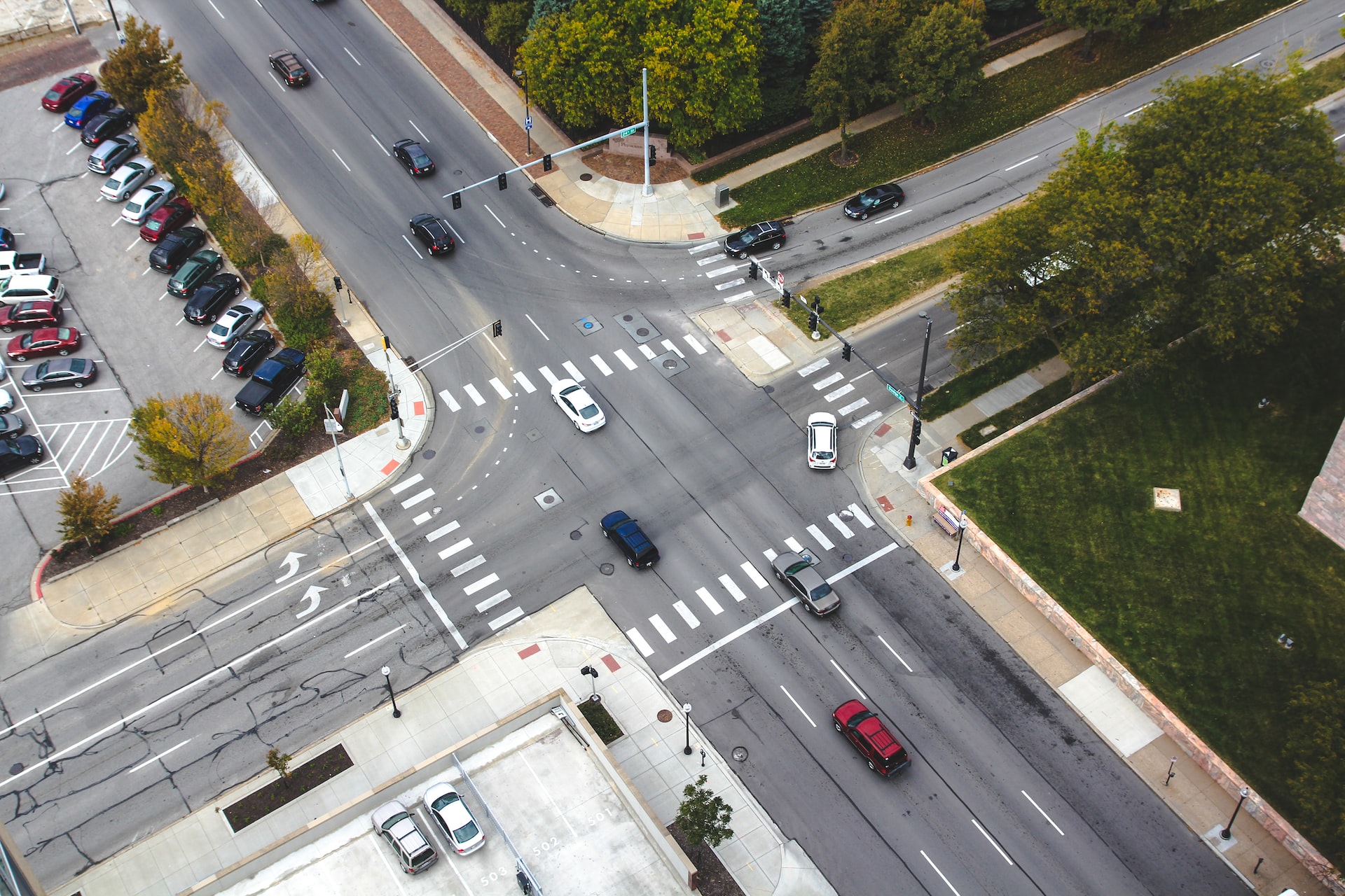 Bird’s-eye view of cars crossing an intersection next to a park with trees