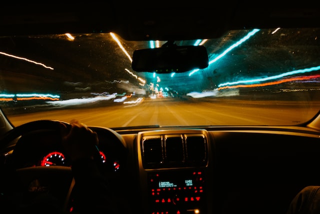 a steering wheel and windshield with a view of blurred lights at night